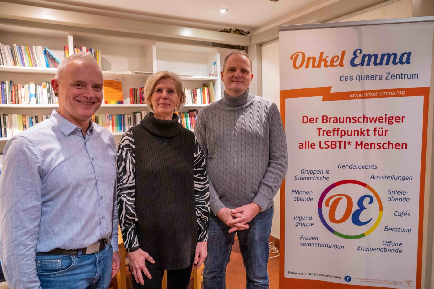 Zwei männliche und eine weibliche Person, darunter Andreas Vogel, CEO von BREDEX, stehen im Onkel Emma, dem queeren Zentrum von Braunschweig vor einem einem Banner des selben Zentrums.