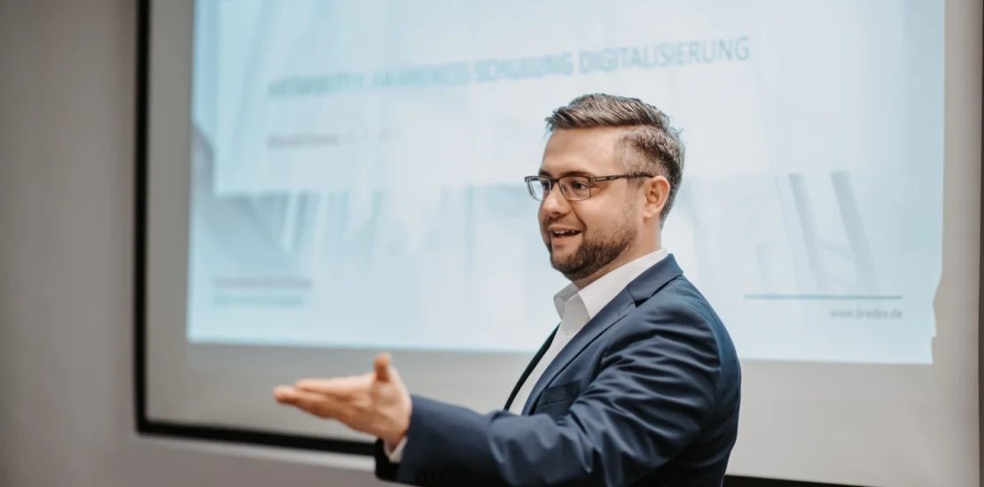 Datenschutzbeauftragter Manuel Strohof, ein Mann mittleren Alters im Anzug und mit dunklen Haaren, steht vor einem Screenboard.