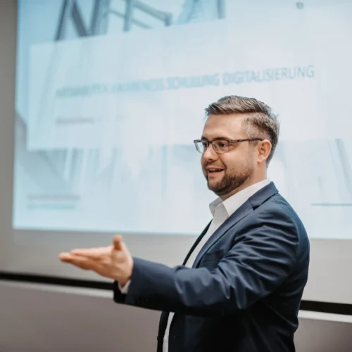 Datenschutzbeauftragter Manuel Strohof, ein Mann mittleren Alters im Anzug und mit dunklen Haaren, steht vor einem Screenboard.