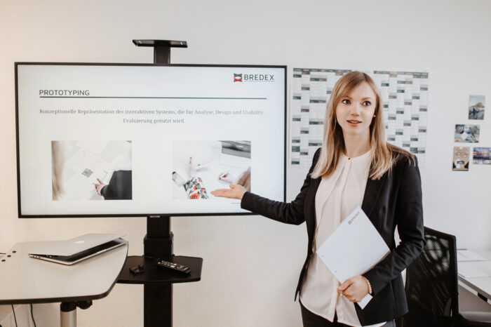 Magdalena Maciejko, UX/UI-Expertin bei BREDEX, steht vor einem Monitor auf dem eine Seite zum Thema Prototyping abgebildet ist.