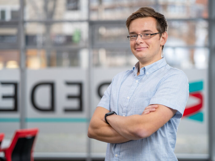 Trainer Christian Rucinski von BREDEX. Ein junger Mann mit braunen Haaren und einer eckigen Brille.