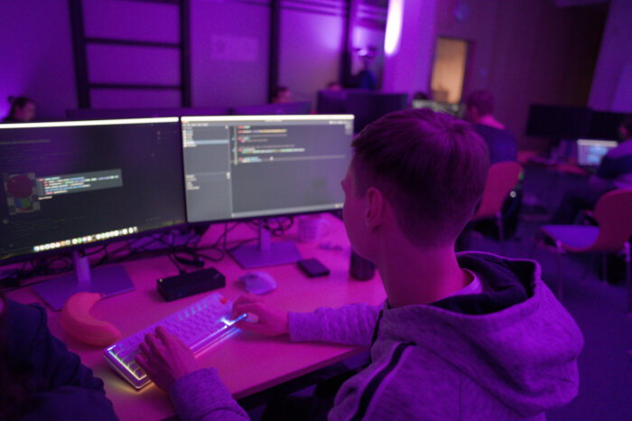 Ein Teilnehmer des Global Game Jam bei BREEX sitzt vor zwei Monitoren und arbeitet an dem Code für ein Computerspiel.